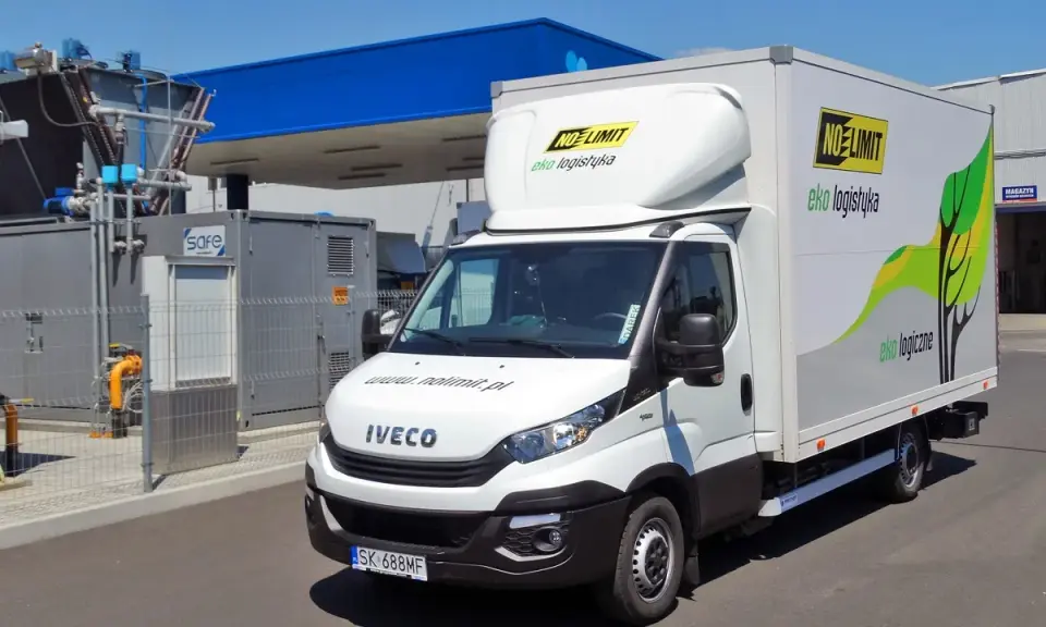 Biała ciężarówka Iveco zasilana gazem CNG, z logo "NO LIMIT eko logistyka", zaparkowana przy stacji paliw.