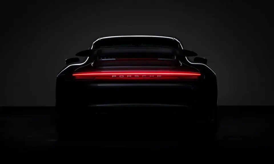 Ein schwarzer Porsche von hinten, dessen Rückleuchten in einem leuchtenden Rot erstrahlen und den Schriftzug "PORSCHE" beleuchten.