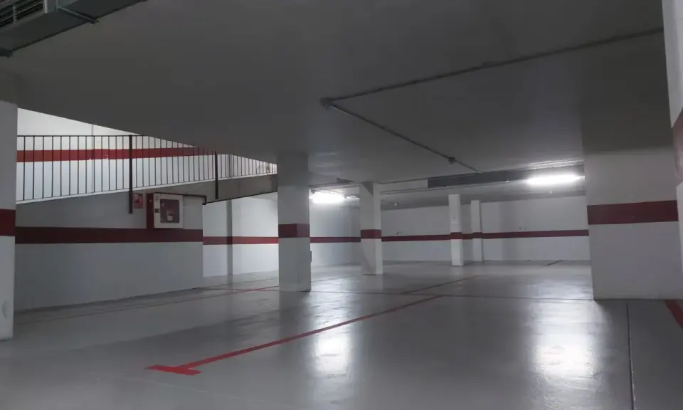 Suelo de garaje recién pintado, con líneas rojas y grises que marcan las plazas.