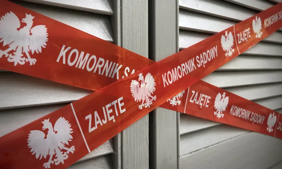 Czerwona taśma z napisem "KOMORNIK SĄDOWY" i godłem Polski krzyżuje się na szarej powierzchni. Jak pozbyć się komornika z konta?