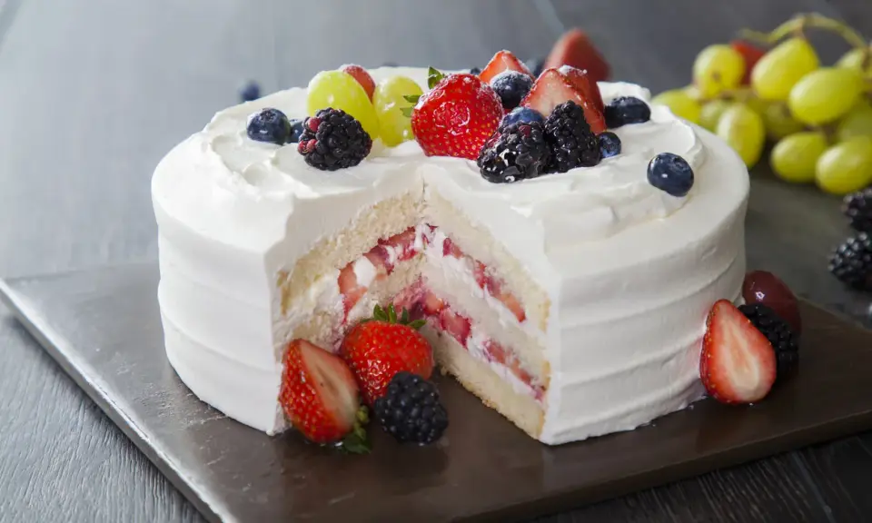 Pyszny tort z bitą śmietaną i mascarpone, przełożony truskawkami i owocami leśnymi. Udekorowany świeżymi owocami.