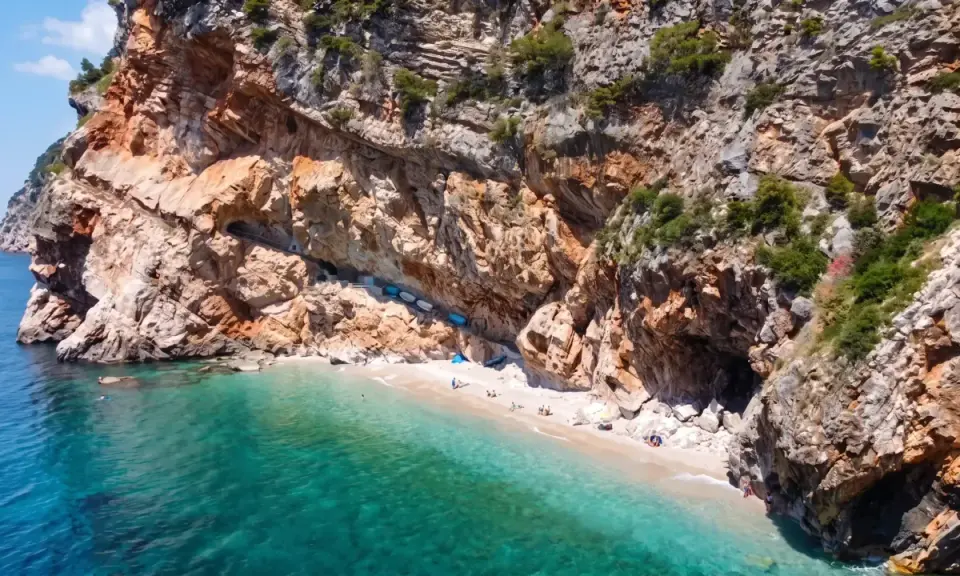 Versteckter geheimtipp kroatien strand: Eine kleine Bucht mit türkisfarbenem Wasser, umgeben von steilen Felsen. Einige Boote liegen am Ufer, wenige Menschen genießen die Ruhe.