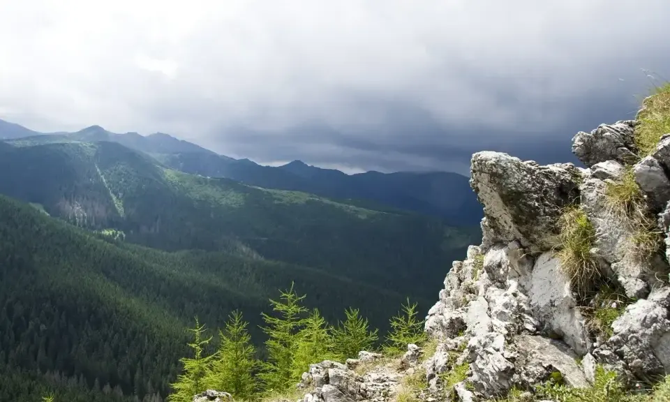 Skalisty szczyt w Zakopanem z widokiem na gęsto zalesione doliny Tatr pod burzowym niebem.
