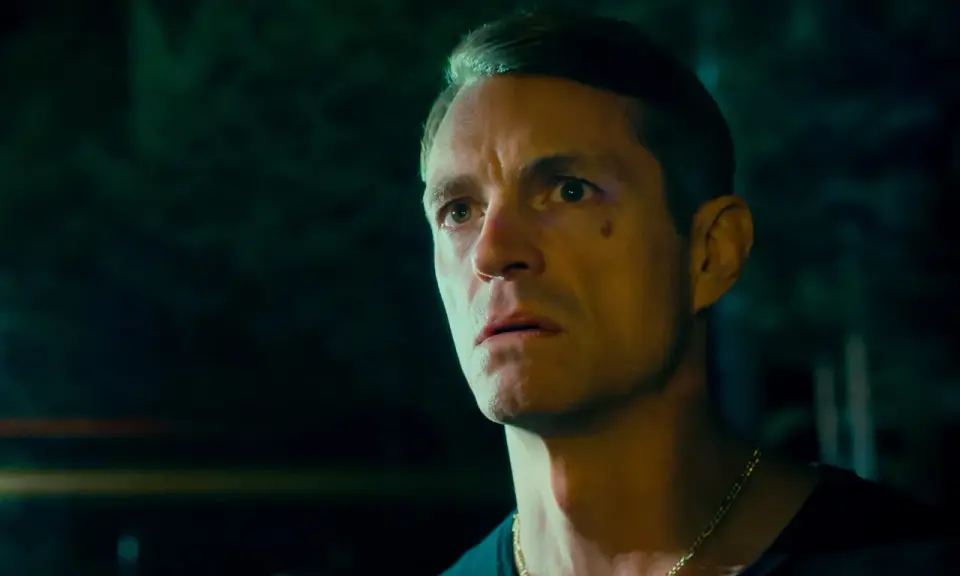 Joel Kinnaman i en mörk, intensiv scen från sin nya serie. Hans blick är fäst på något utanför bild, full av oro och beslutsamhet.