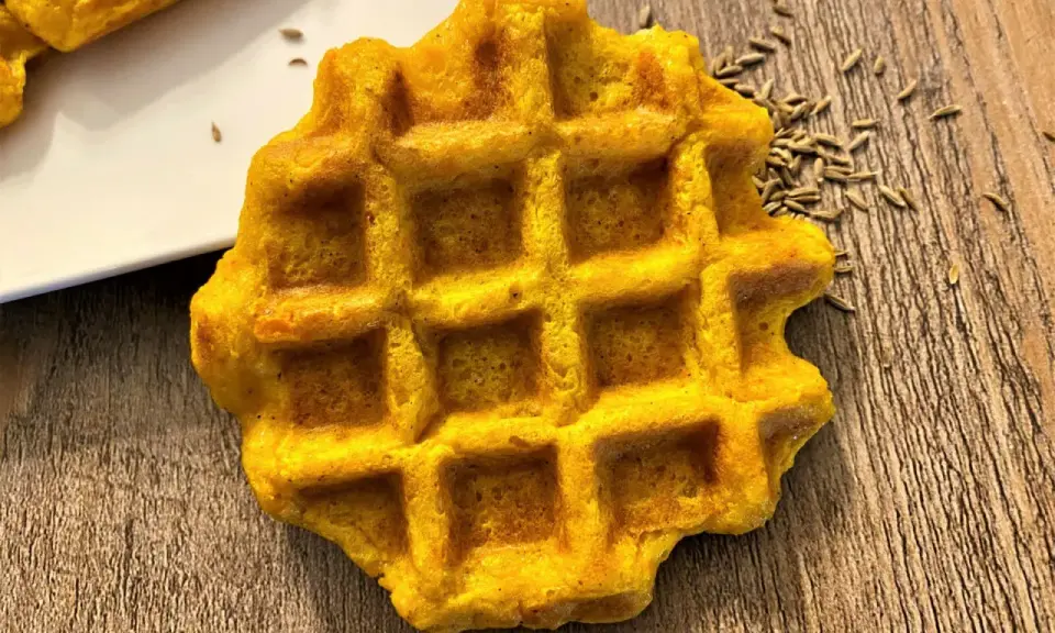 Gaufre carotte dorée, parsemée de graines sur fond de bois. Un délice orangé à déguster.