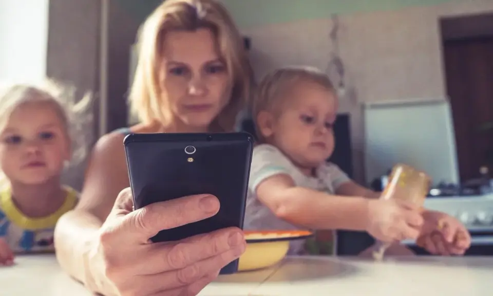 Madre con su móvil, mientras sus hijos pequeños, de unos 2 años, miran pantallas.