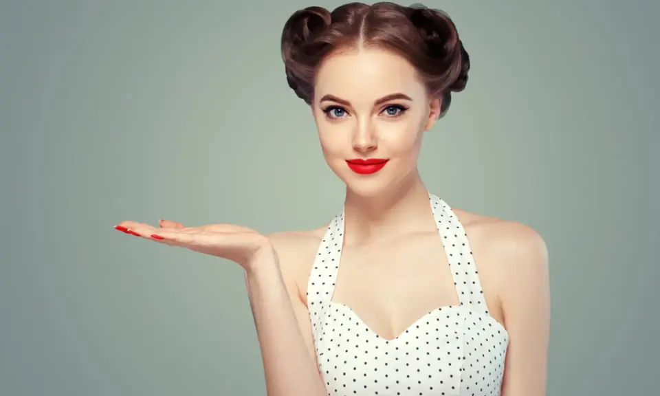 Kobieta w stylu pin up, z burzą loków i czerwoną szminką, prezentuje dłoń. To lata 50. w pełnej krasie.