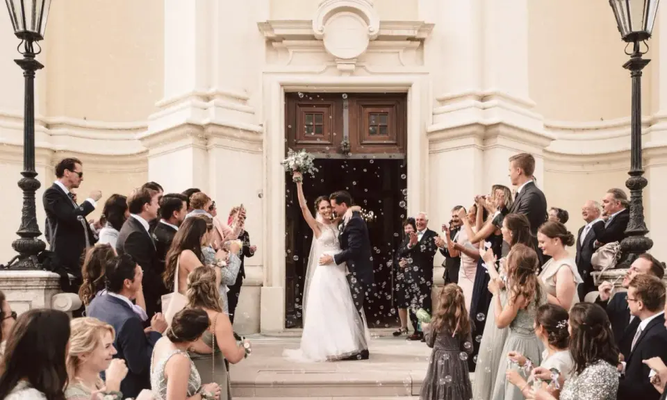 Ein strahlendes Brautpaar verlässt die Kirche, umgeben von Seifenblasen und jubelnden Gästen. Eine klassische Hochzeit voller Freude und Romantik.