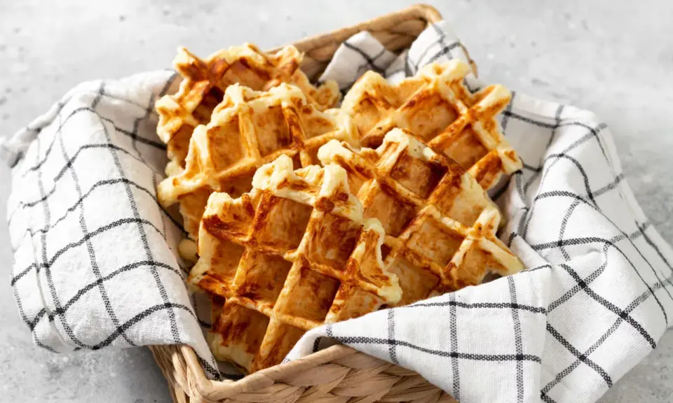 Un panier rempli de gaufres dorées, parfaites pour une recette gaufre rapide. Elles sont présentées sur une serviette à carreaux noirs et blancs.