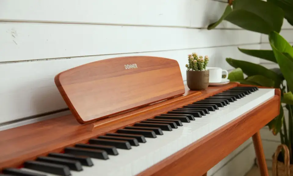 Eleganckie pianino cyfrowe Donner, idealne do nauki gry na pianinie online. Obok stoi filiżanka kawy i mała roślinka.