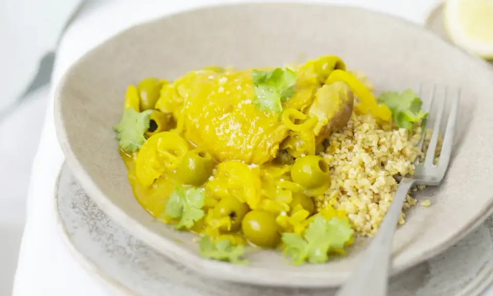 Un plat de tajine poulet citron, garni d'olives vertes et de coriandre fraîche, servi avec du couscous.