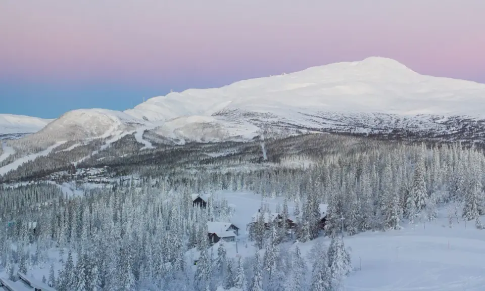 Snötäckta berg och skog med små stugor, en idyllisk vy över mindre skidorter Sverige i skymningen.