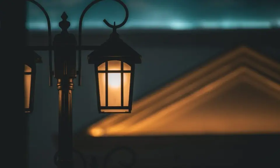 Ciepłe światło zabytkowych lamp miejskich rozświetla zmierzch, rzucając geometryczne cienie na budynek.