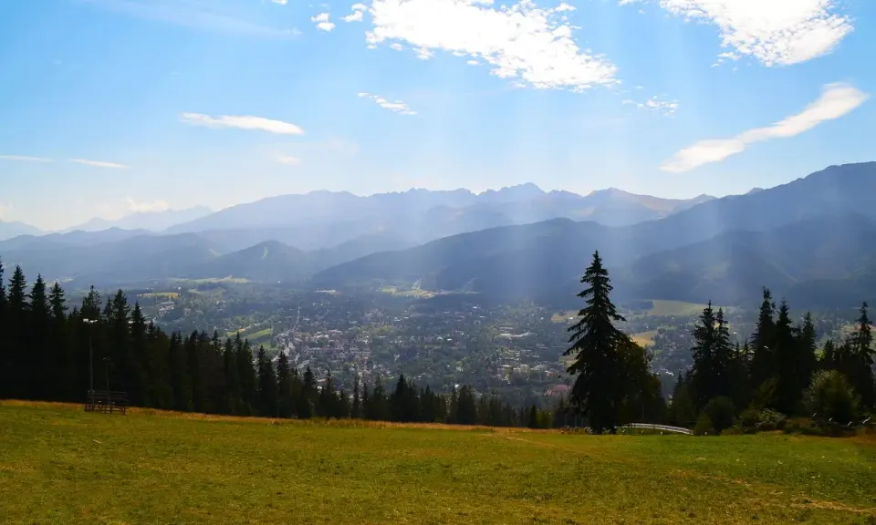 Widok na Zakopane z Gubałówki. Słońce przebija się przez chmury, oświetlając miasto i góry. Zastanawiasz się, ile się idzie na Gubałówkę?