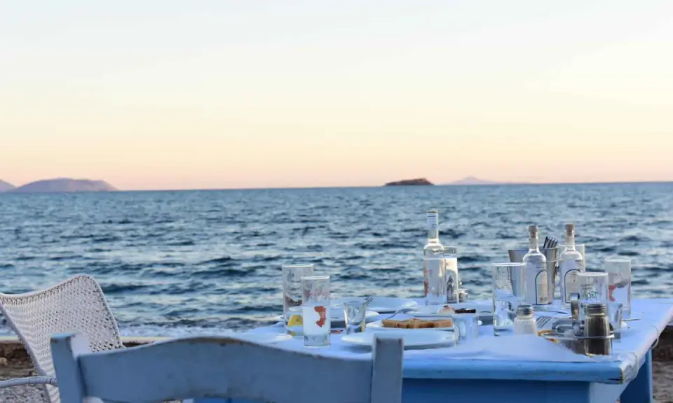 Tisch am Meer mit Ouzo-Flaschen, Gläsern und Essen. Der Ouzo-Prozent ist perfekt für den Sonnenuntergang.