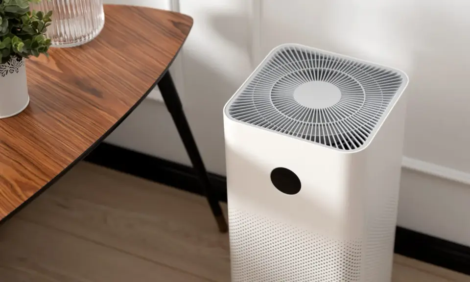 Purificador de aire blanco junto a una mesa de madera. Muestra cómo funciona un purificador de aire al aspirar y limpiar el aire.