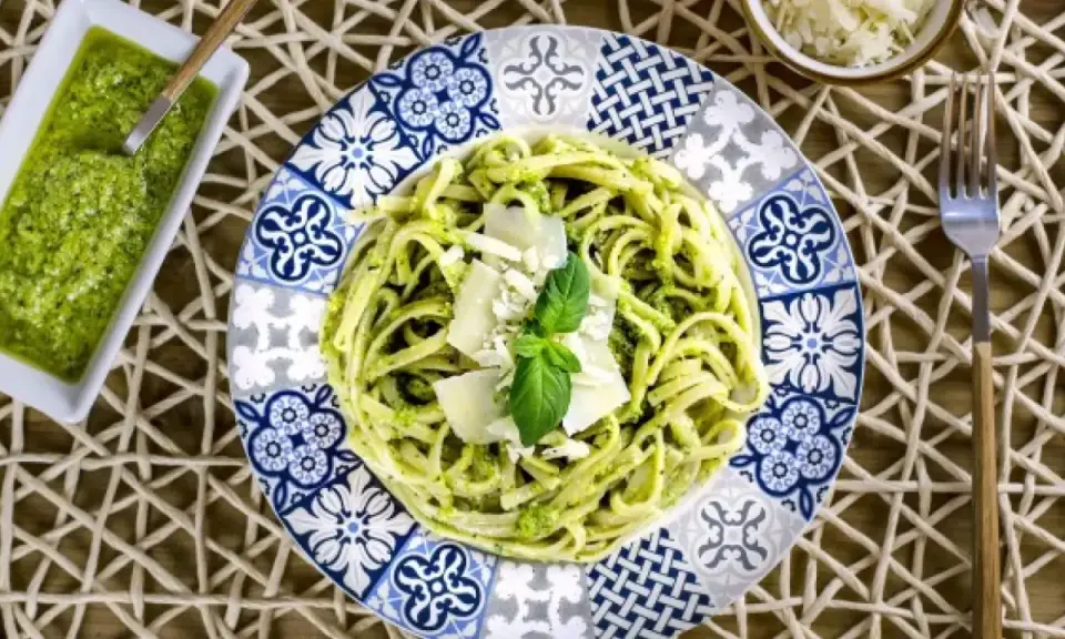 Deliciosa pasta con pesto, ideal para tus recetas de pasta con pesto. Servida en un plato decorado con un toque mediterráneo.