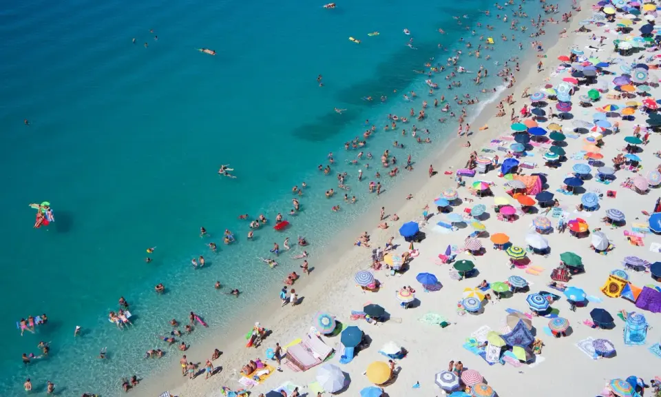 Spiaggia affollata con ombrelloni colorati e bagnanti nell'acqua cristallina, un'immagine perfetta per scoprire le località di mare più economiche in Italia.