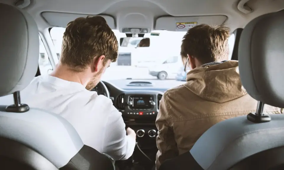 Dos hombres en un coche, uno conduce y el otro mira. Podrían estar discutiendo los tipos de faltas que se cometen al volante.