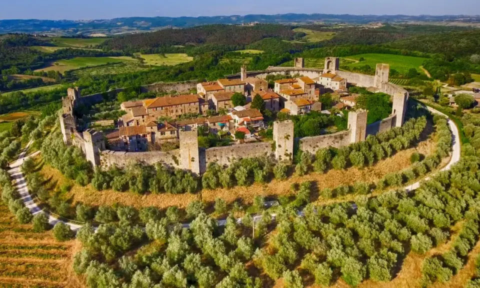 Borgo medievale fortificato su una collina, circondato da uliveti e vigneti. Bellissimi paesaggi toscani sotto un cielo azzurro.