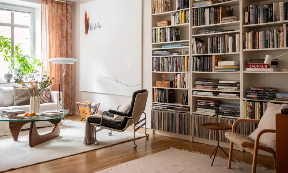 Acogedora sala de estar con una estantería repleta de libros, vinilos y objetos decorativos. La **decoración de librería** se integra perfectamente con el mobiliario moderno y la luz natural.