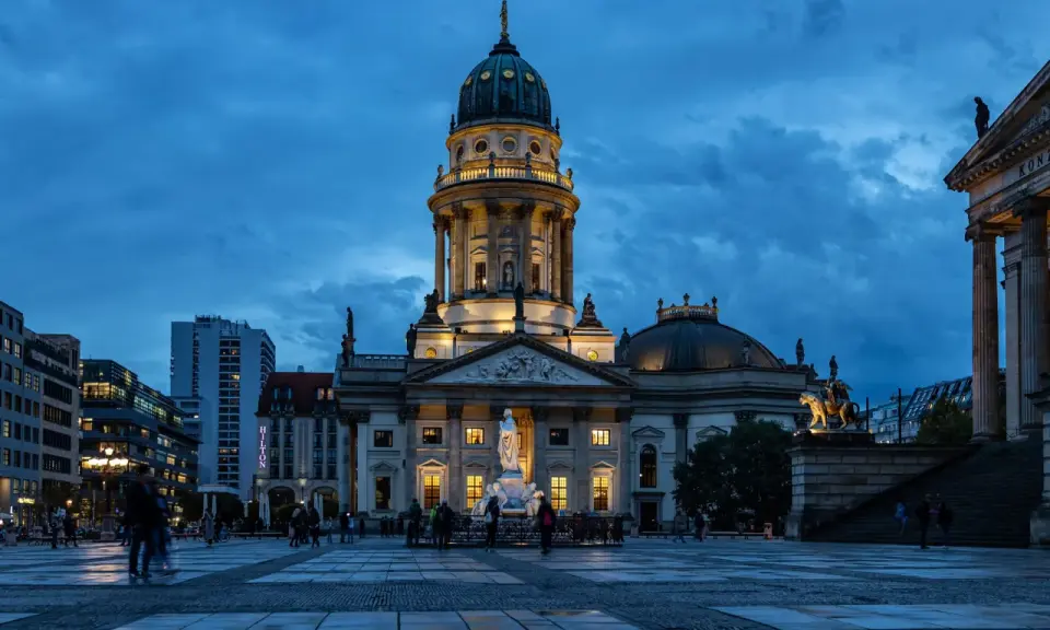 Der Gendarmenmarkt in Berlin bei Dämmerung. Die Kuppeln des Deutschen und Französischen Doms, Zeugen der Hugenotten in Berlin, erstrahlen im Licht.