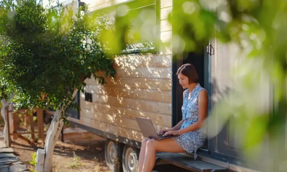 Frau arbeitet auf Laptop vor einem Tiny House. Ein Beispiel für modernes, flexibles wohnen in der zukunft.