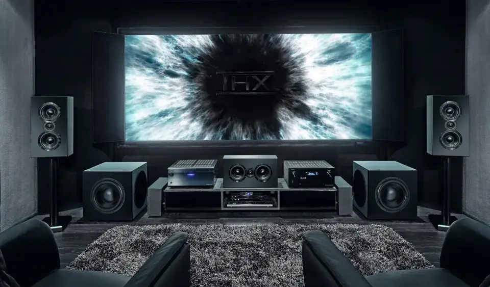 Installation home cinema avec écran THX, amplificateur, enceintes et fauteuils en cuir noir pour une expérience immersive.