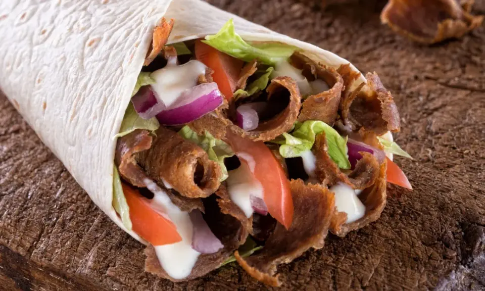 Pyszny, domowy kebab zawinięty w tortillę z soczystym mięsem, chrupiącą sałatą, pomidorami i cebulą, polany sosem.
