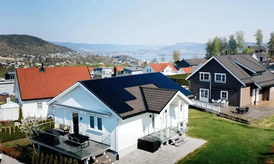 Vackra hus med solpaneler på taken, en del av ett system med Growatt 8000TL3-XH, i ett soligt bostadsområde med utsikt över en sjö.