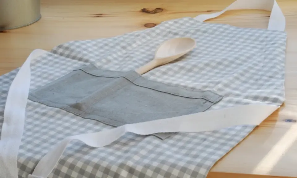 Gotowy fartuch kuchenny w kratkę, z drewnianą łyżką w kieszeni. Idealny poradnik, jak uszyć fartuch kuchenny.