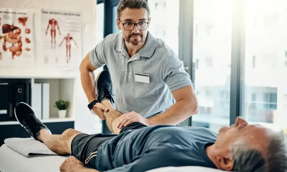 Fizjoterapeuta ćwiczy nogę starszego pacjenta. Rehabilitacja jest kluczowa, by dowiedzieć się, komu przysługuje szpital uzdrowiskowy.