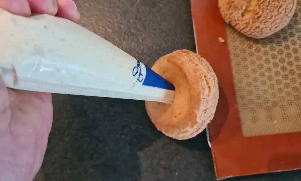 Garnissage d'une pâte à choux profiterole avec une crème onctueuse à l'aide d'une poche à douille.