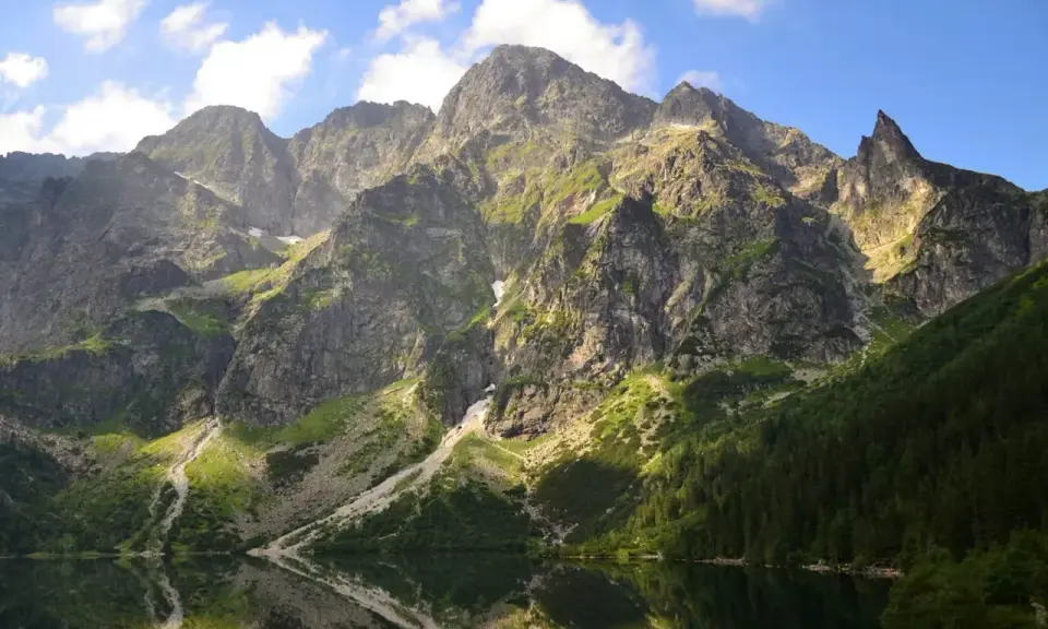 Majestätische Berge im Tatra Gebirge laden zum Wandern ein. Ein ruhiger See spiegelt die felsigen Hänge und den blauen Himmel wider.