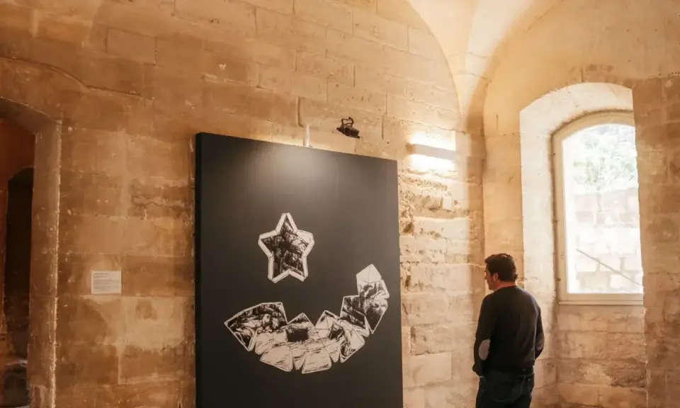 Un homme admire une œuvre d'art abstraite lors d'une expo Avignon. La pièce représente une étoile au-dessus d'une forme souriante composée de fragments.