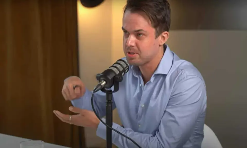 Michael van de Poppe w niebieskiej koszuli mówi do mikrofonu, gestykulując.