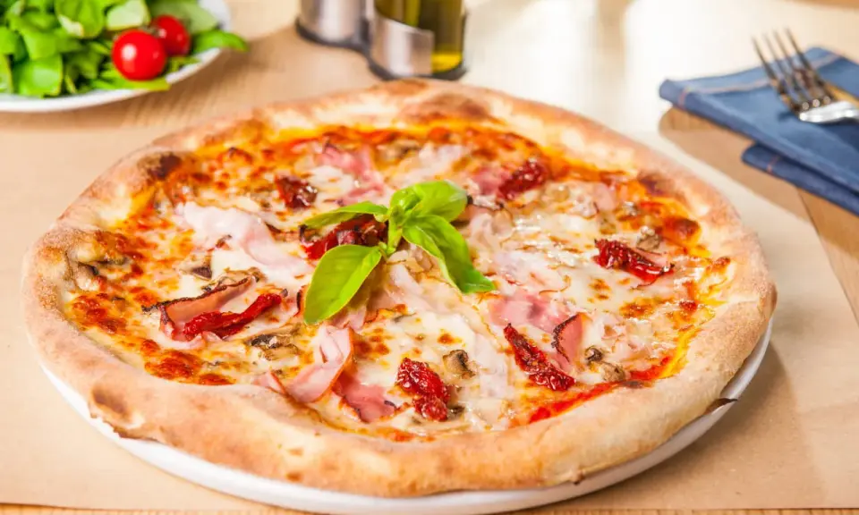Une délicieuse pizza garnie de jambon, de tomates séchées et de champignons, avec une pousse de pâte à pizza bien dorée.