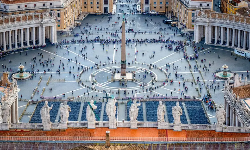 Vue aérienne de la **place du Vatican**, avec son obélisque central, ses fontaines et une foule de visiteurs.