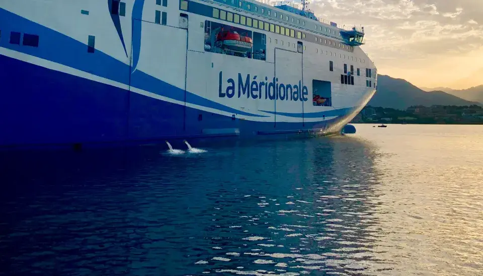 Le ferry "La Méridionale" se prépare à partir, le ballast navire est ajusté pour la traversée. L'eau reflète le ciel doré.
