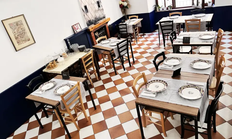 Tavoli apparecchiati in un ristorante, pronti per un'esperienza di **mangiare in Umbria**. Pavimento a scacchi, sedie in legno e dettagli eleganti.