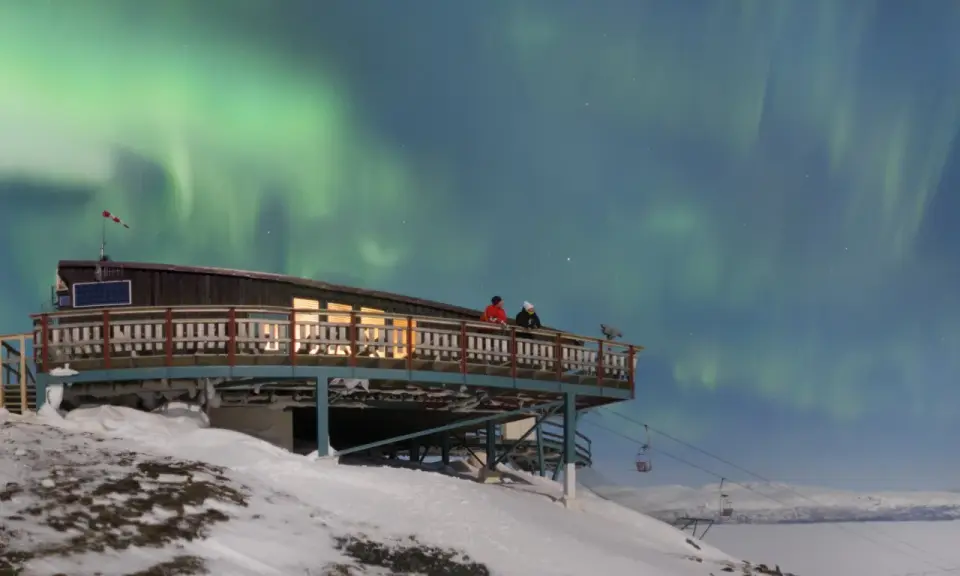 Två personer njuter av norrskenet från en aurora sky station i snöig fjällmiljö.