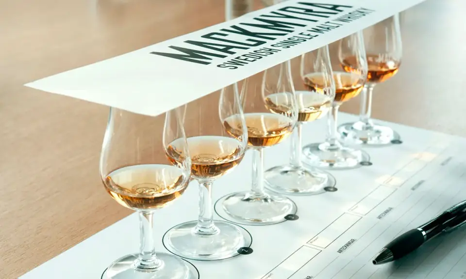 Mackmyra whiskyprovning med sex glas gyllene whisky uppradade på ett bord. En penna ligger redo för anteckningar.