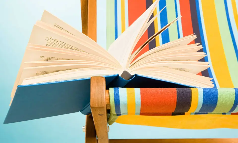 Un libro aperto, pieno di classici della letteratura, appoggiato su una sdraio a righe colorate.