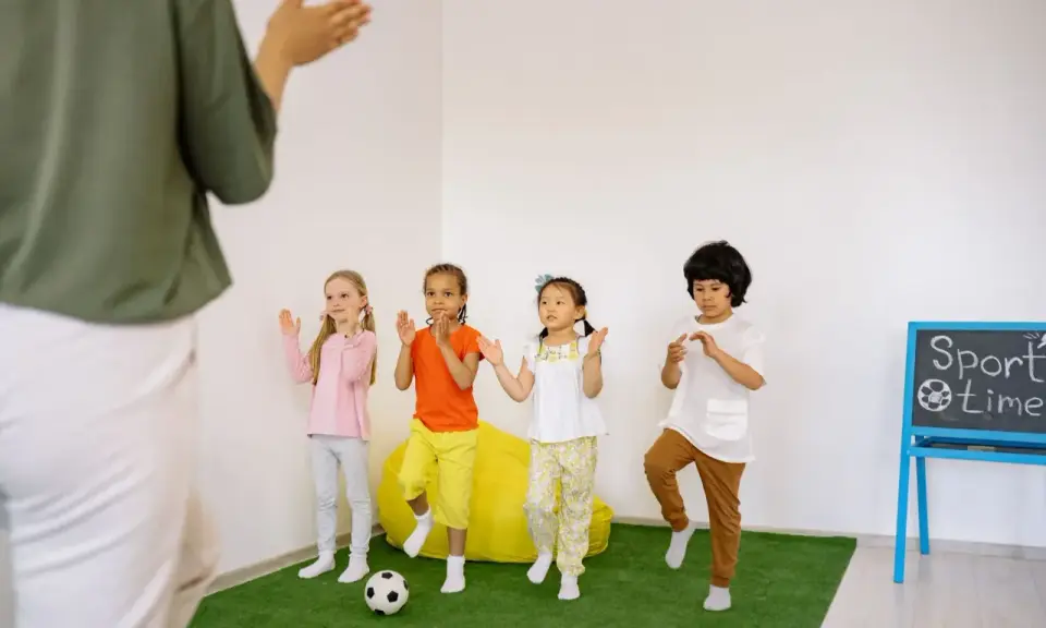 Dzieci ćwiczą przy tablicy z napisem "Sport time". Krótkie hasła sportowe dla dzieci motywują do ruchu.