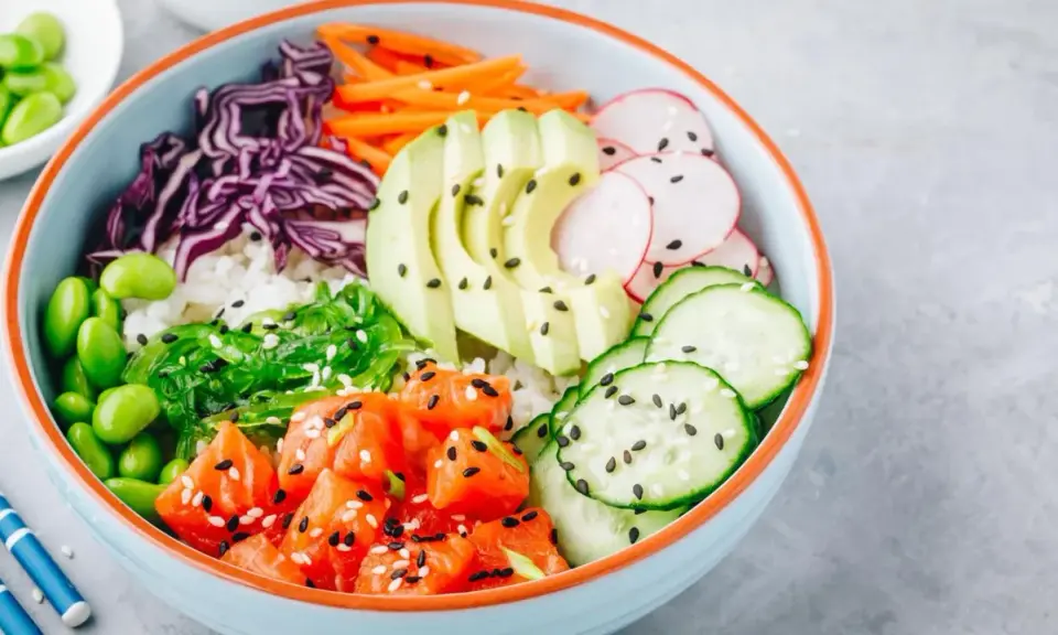 Eine bunte Poke Bowl mit Lachs, Avocado, Edamame, Rotkohl, Gurke, Radieschen und Seetang.