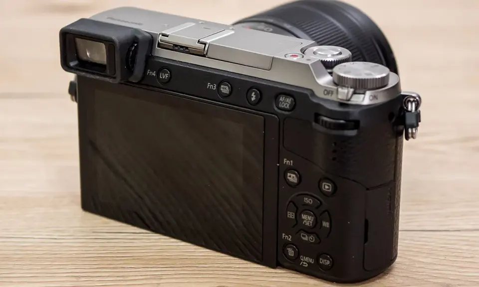 Retro della fotocamera Panasonic Lumix GX80 con obiettivo. Schermo LCD e mirino elettronico visibili.