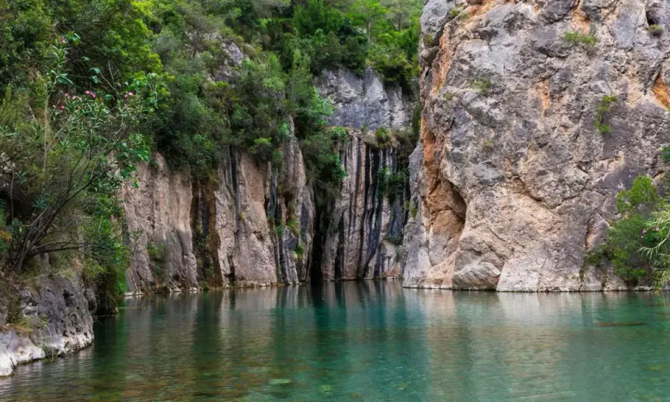 Aguas cristalinas reflejan imponentes rocas y vegetación exuberante en estas piscinas naturales de Castellón. Un rincón idílico para refrescarse.