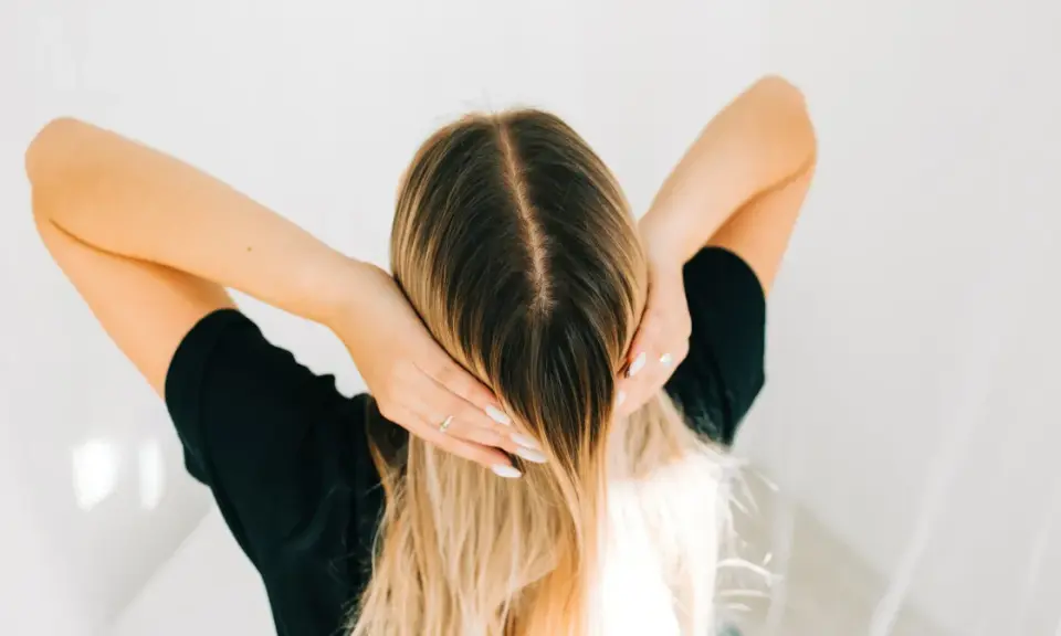 Kobieta z blond włosami, która delikatnie dotyka swojej głowy, jakby stosowała krople żołądkowe na włosy dla ich wzmocnienia.