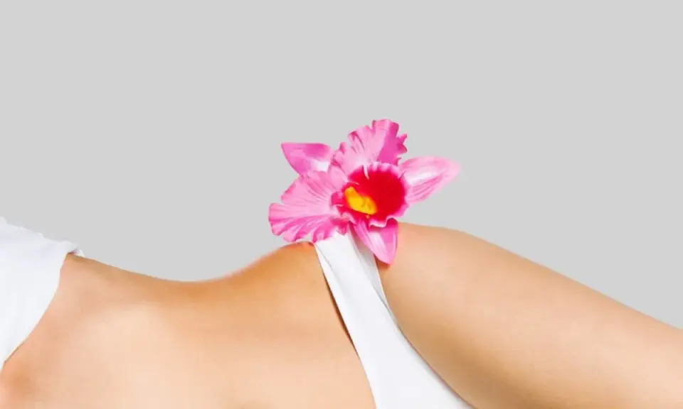 Delikatna różowa orchidea na tle kobiecego ciała, symbolizująca naturalne piękno i różnorodne rodzaje warg sromowych.
