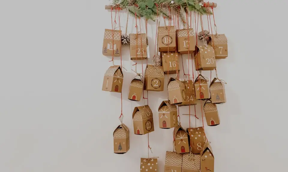 Uroczy pomysł na kalendarz adwentowy: zawieszone na gałęzi ozdobionej gałązkami jodły, małe, brązowe pudełeczka z numerami od 1 do 24.